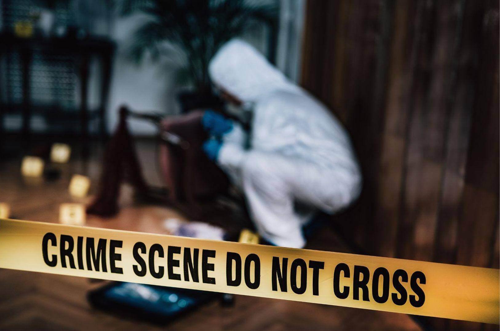 A crime scene investigator in a hazmat suit behind yellow crime scene tape in an apartment building in Carrollton, Georgia