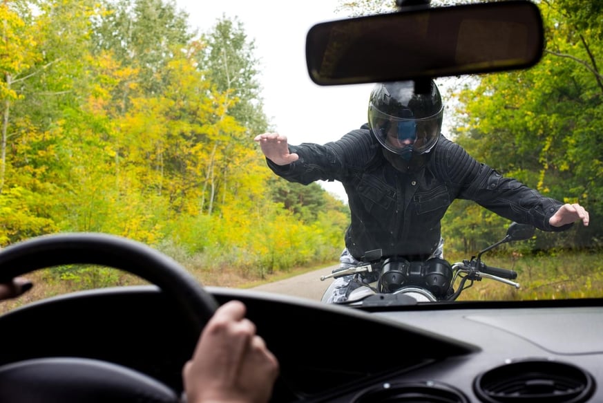 A motorcyclist seen through a car windshield dead on who is trying to slow himself before being hit in Duluth, Georgia
