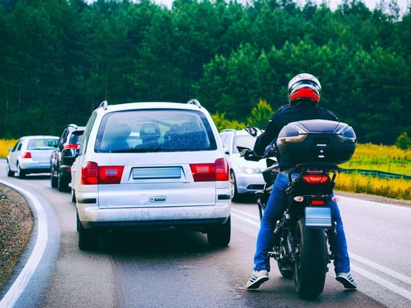 Motorcycle rider driving behind a hatchback on a busy roadway