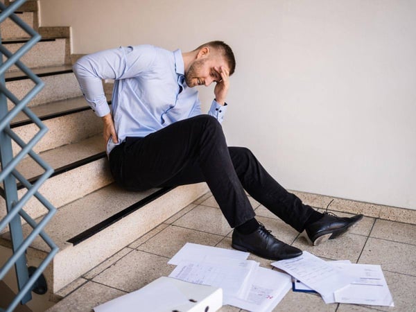 A male office worker experiencing lower back pain after falling down office stairs. 